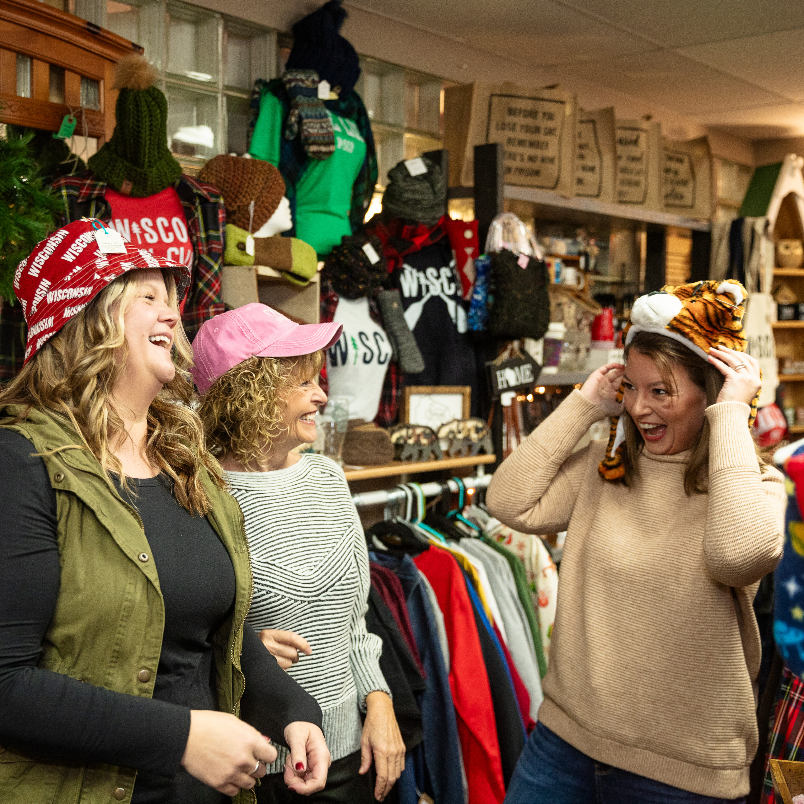 Three women shopping at a local store, laughing together as they try on hats