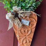 A decorative carrot shaped door hanger with greens and ribbon