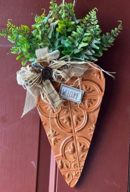 A decorative carrot shaped door hanger with greens and ribbon