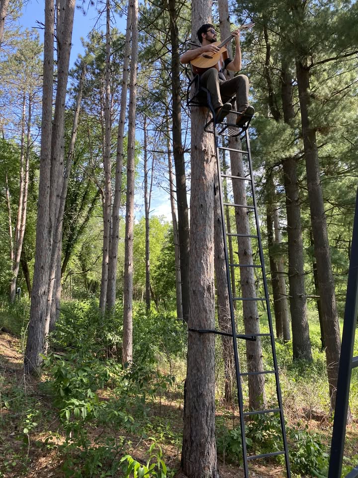 Colton Warren with guitar sitting in a tree stand