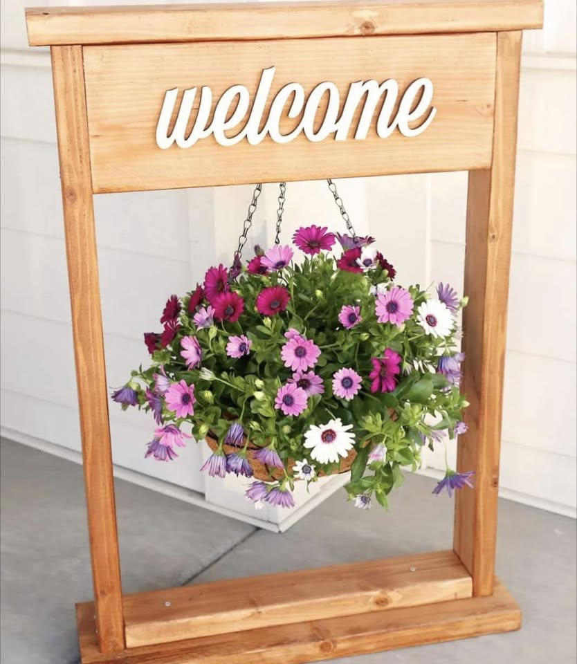 A wooden welcome sign frame with a planter hanging off of it.