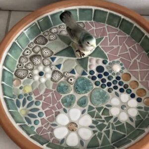 A picture of a Dark green, white, gray bird bath with a fake gray and white bird in it.