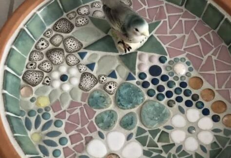 A picture of a Dark green, white, gray bird bath with a fake gray and white bird in it.