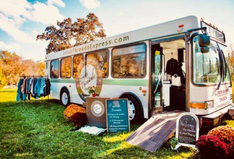 A bus with clothes on the side of it and signs with the event information on it.