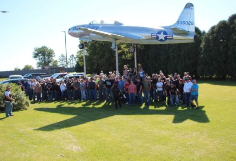 A photo of a group of people posing in front of a army plane.