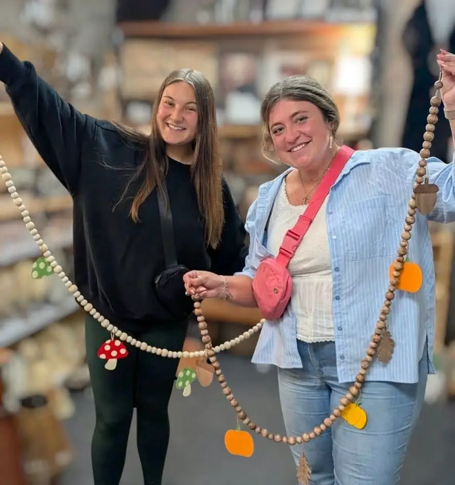 Two women hold up their fall themed beaded garlands