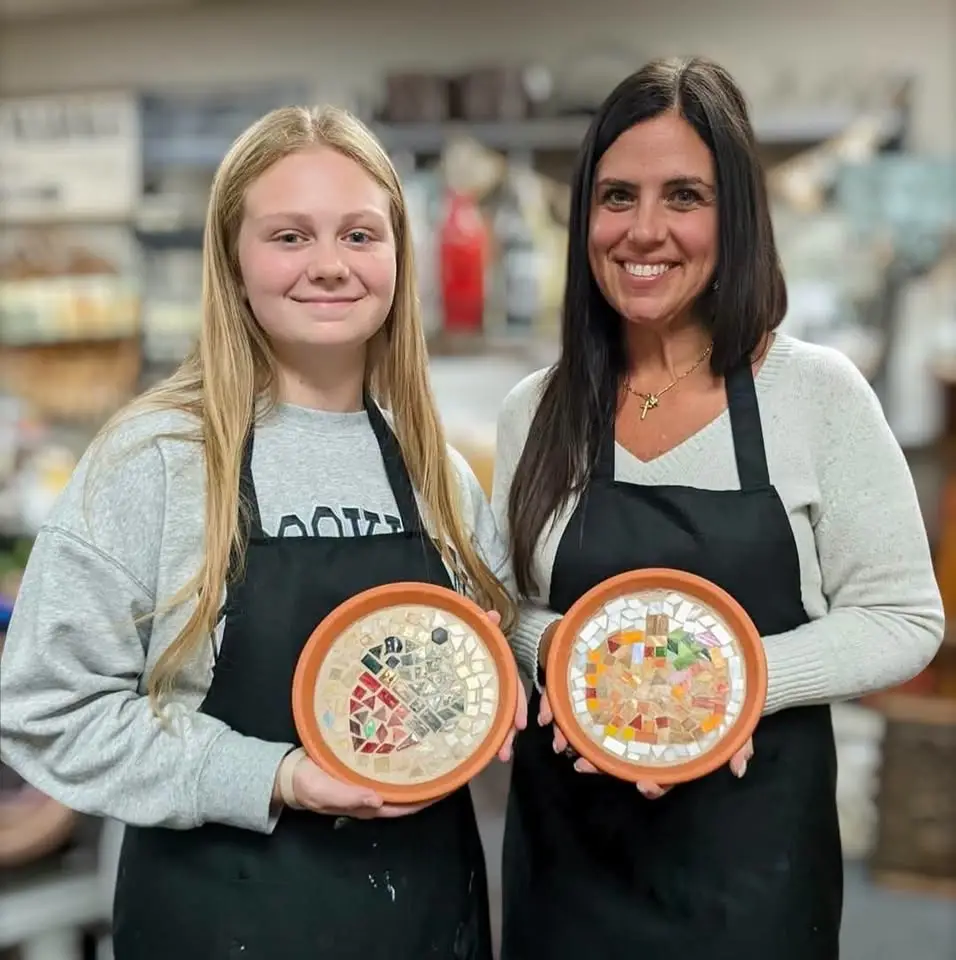 two women holding their mosaic decorative trays