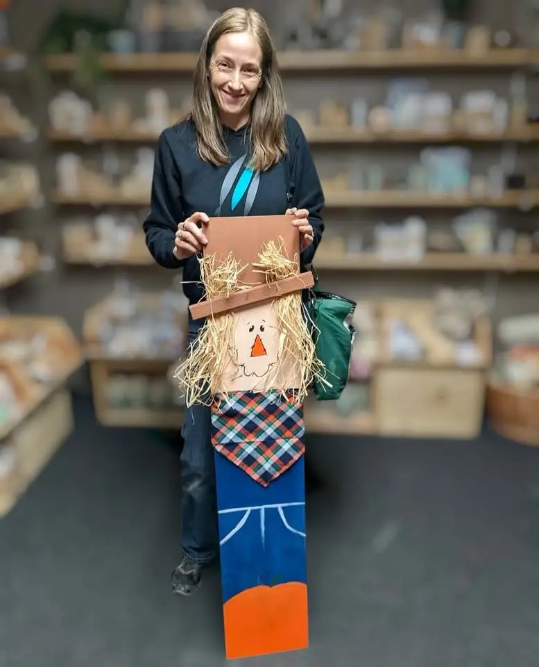 A woman stands with her wooden scarecrow