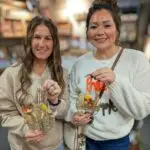 two women hold their small dried floral wall hangs