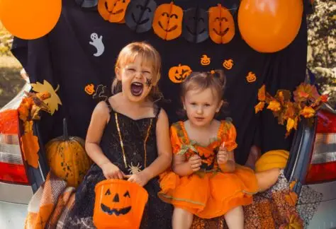 Children sitting on a car bumper with the trunk open dressed in halloween outfits